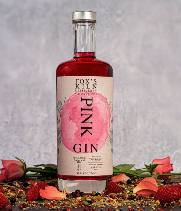 Fox's Kiln Pink Gin 70cl bottle surrounded with botanicals in front of a grey background